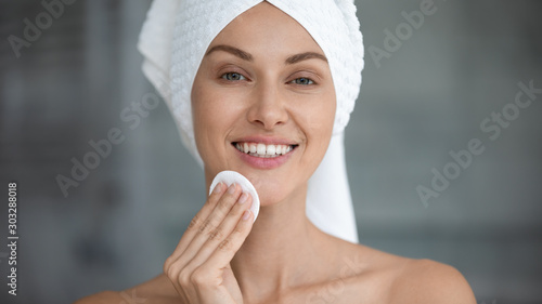 Smiling beautiful woman hold cotton pad cleansing face skin