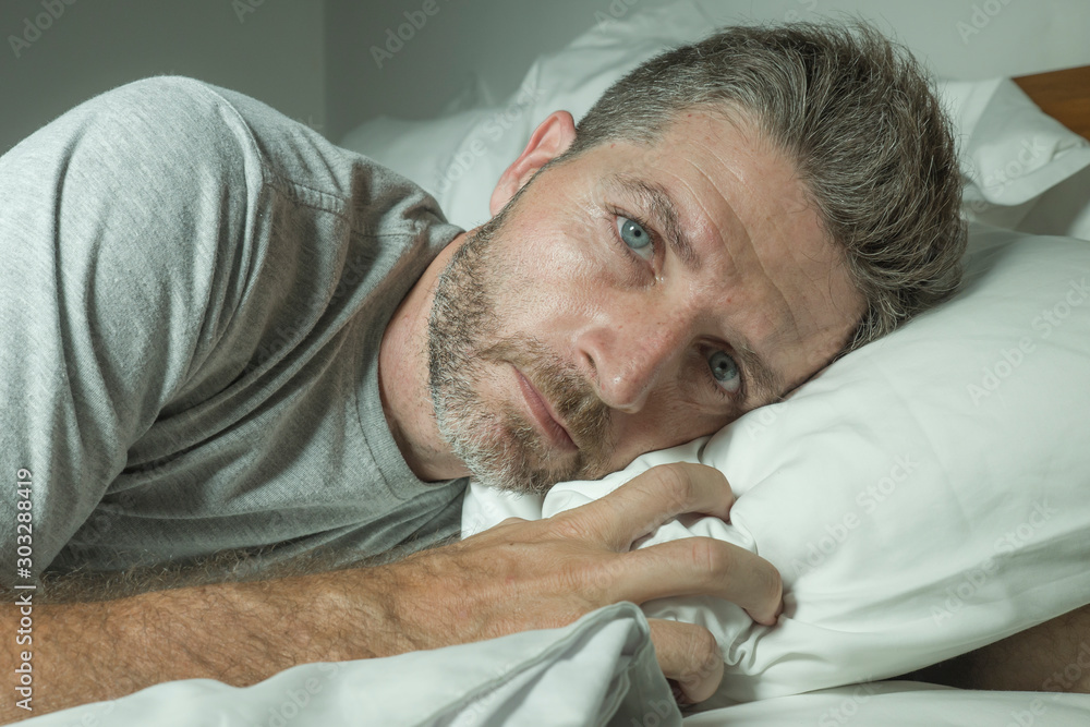 dramatic portrait of stressed and frustrated man in bed awake at night suffering insomnia sleeping disorder tired and desperate unable sleep feeling exhausted - obrazy, fototapety, plakaty 
