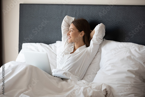 Happy woman relaxing in bed with laptop enjoying good morning