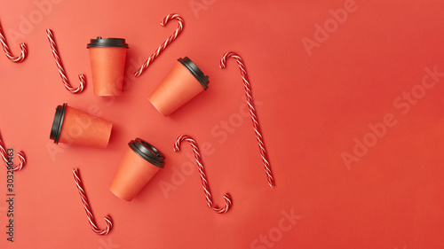 Paper coffee cup with sugar canes on a red background. Christmas background with Xmas candy canes and cofee. Top view, flat lay, mockup. Copy space for text.