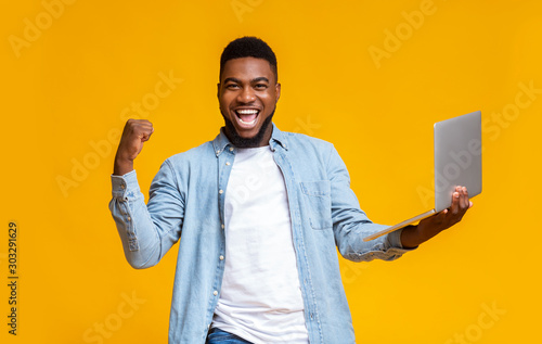 Happy black guy rejoicing success with laptop photo