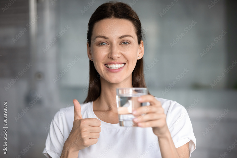Happy attractive woman holding glass of water showing thumbs up Happy attractive woman holding glass of water showing thumbs up