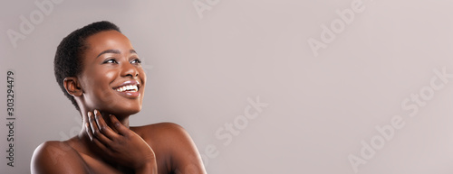 Happy afro woman touching her perfect skin and looking aside photo