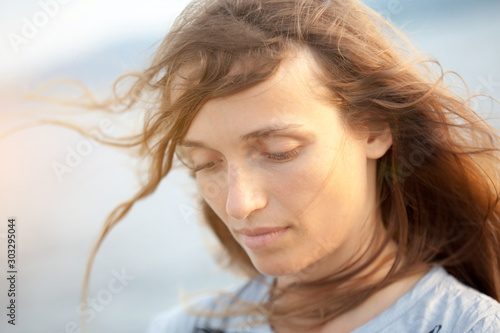 A portrait of a beautiful fair-haired young woman in windy weather near the ocean. Her hair is hanging down on her face.