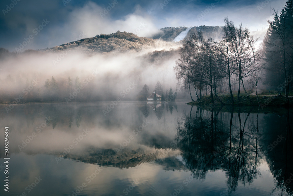 Fototapeta premium Foggy day at a lake with a little island with a church in the middle. Mogoasa, Romania.