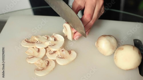 female hands cut champignon mushrooms on a white board background