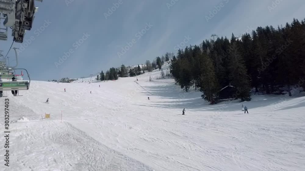 View from a ski lift ascending the mountain on the Krvavec alpine resort in Slovenia, many skiers descent downhill a track to the right View from a ski lift ascending the mountain on the Krvavec alpine resort in Slovenia, many skiers descent downhill a track to the right
