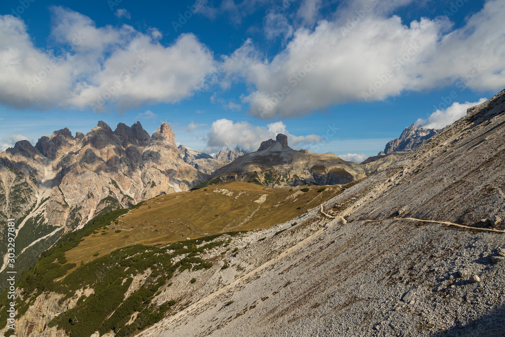View of the mountains and valleys around Tre Cime in the Italian Dolomites. The photo has a nice background with blue sky and white clouds.