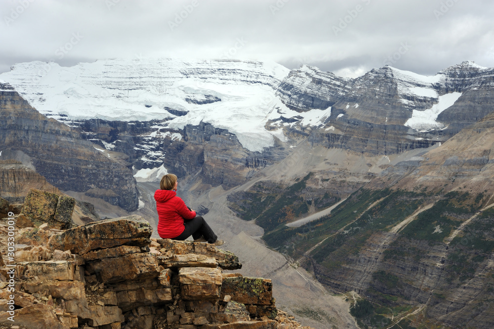 Woman sitting on cliff looking at scenic view of Victoria Glacier. Woman hiking in Canadian Rocky Mountains.  Fairview mountain. Banff National Park. Alberta. Canada.