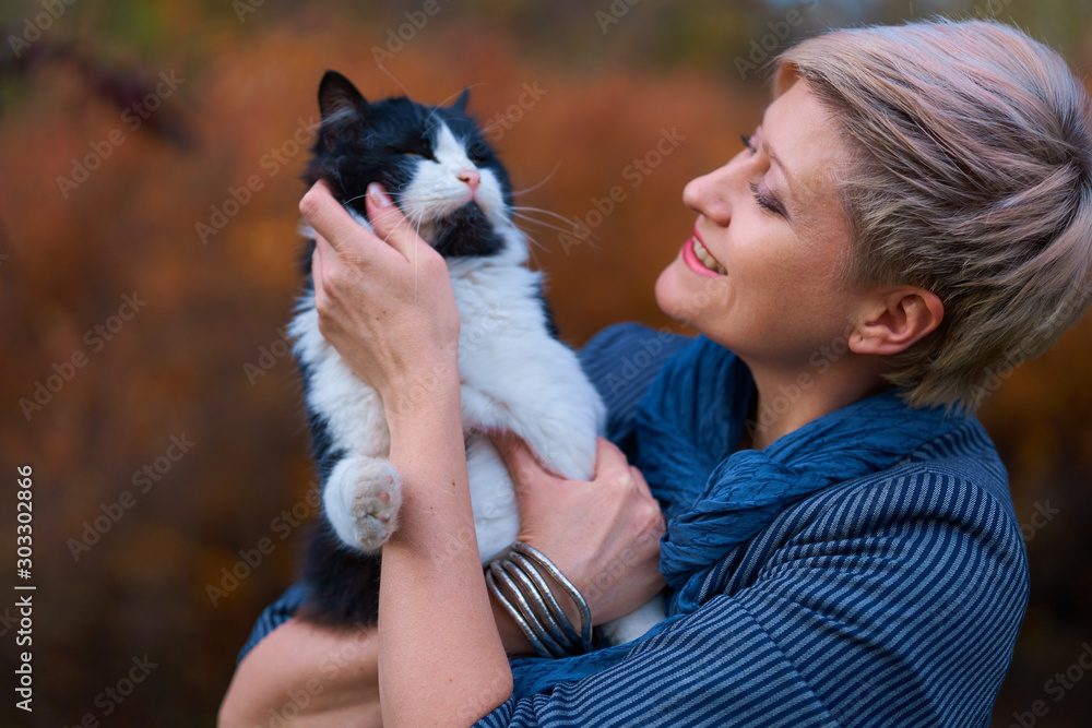 Beautiful elegant blond woman playing with cat in autumn city park, dressed in blue jeans and jacket Beautiful elegant blond woman playing with cat in autumn city park, dressed in blue jeans and jacket