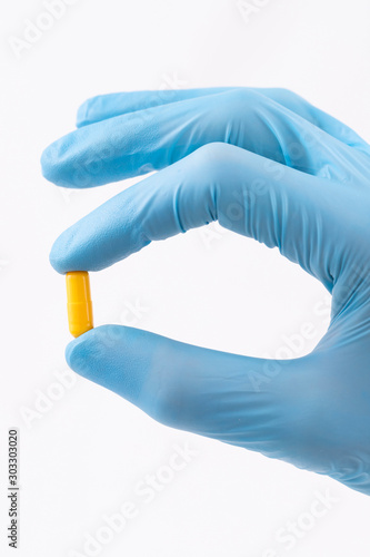 Doctor's hand, weared in blue glove, holding yellow pill (vertical)