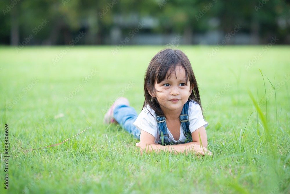 Adorable 3 years old little girl is lying down on the grass field and looking up something during playing time , concept of kid activity. Adorable 3 years old little girl is lying down on the grass field and looking up something during playing time , concept of kid activity.