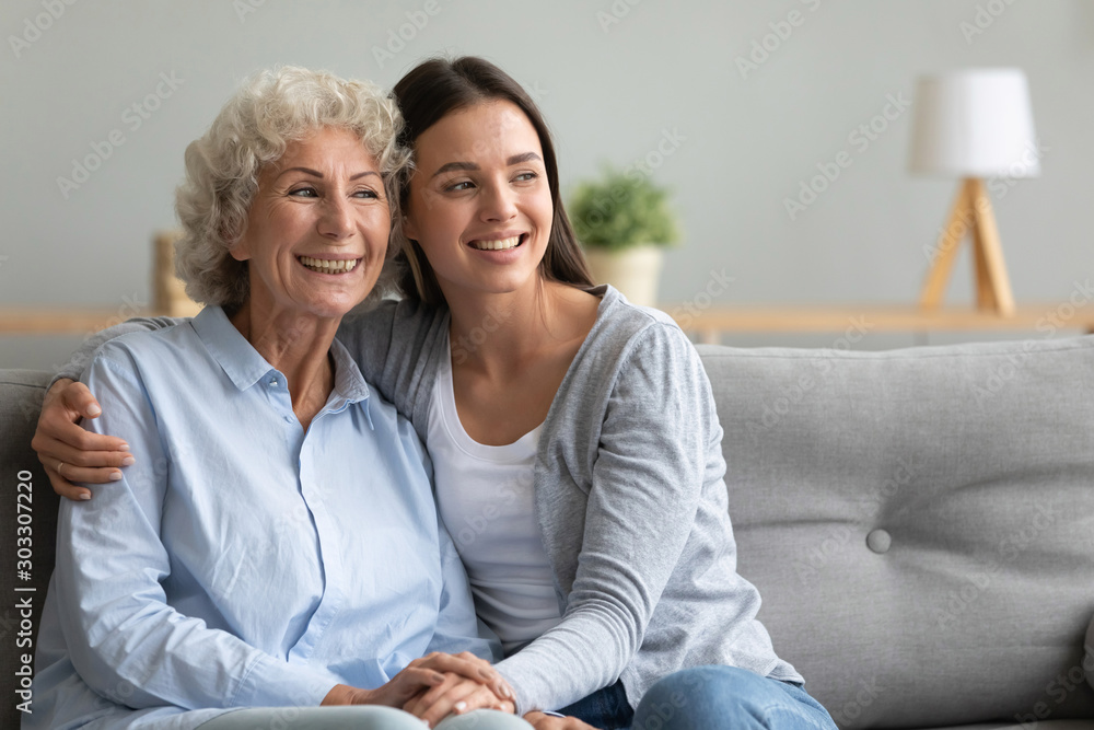 Caring young granddaughter hug old grandmother bonding looking away Caring young granddaughter hug old grandmother bonding looking away