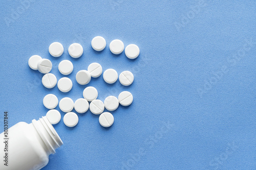 Bottle with white vitamin pills scattered on a blue background.