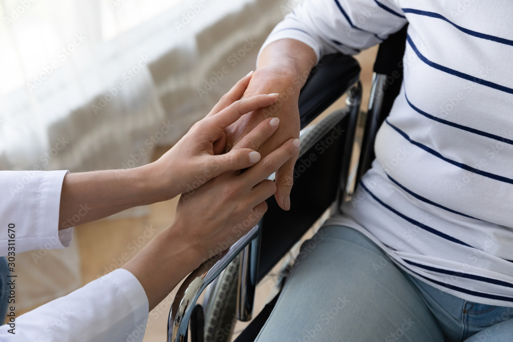Nurse hold hand support handicapped senior patient on wheelchair, closeup