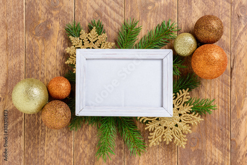 Photo frame between Christmas decoration, with multicolored balls and snowflakes on a brown wooden table. Top view, frame to copy space
