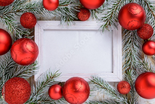 Photo frame between Christmas decoration, with red balls on a white wooden table. Top view, frame to copy space
