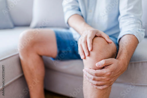 Man suffering from knee pain sitting sofa photo