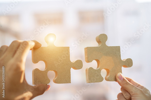 hands connecting couple puzzle piece against sunrise effect, businesswoman and business man holding wood jigsaw with sunset background. Business solutions, target, success, goals and strategy concepts