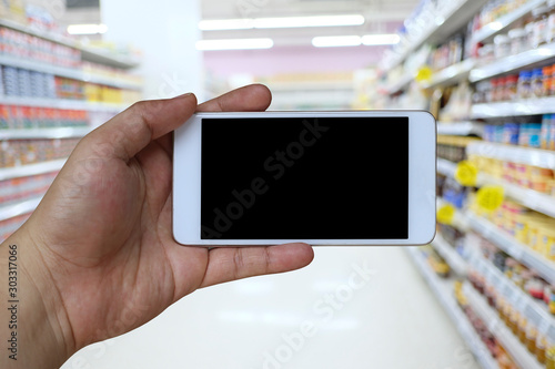Hand of a man holding smartphone device in the supermarket background.