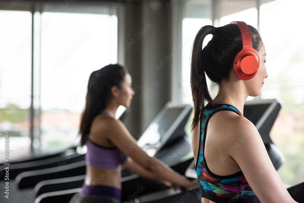 Obraz premium Side View Of Smiling Young Woman Wearing Red Headphones While Exercising On Treadmill In Gym