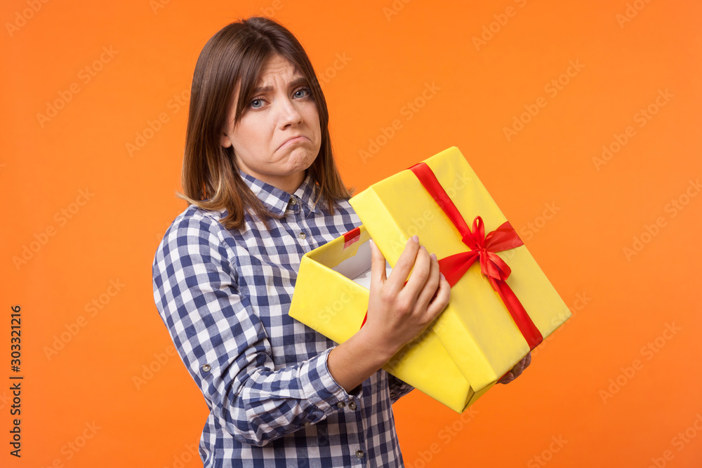 Φωτογραφία Portrait of unhappy young woman with brown hair in casual checkered shirt holding gift box, looking disappointed at camera, dissatisfied with present