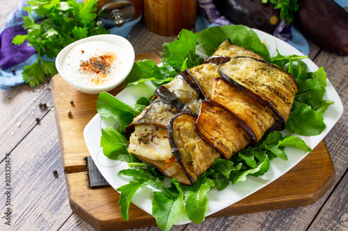 Tasty fish baked with vegetables in eggplant, served with paprika yogurt sauce on a wooden table. Copy space.