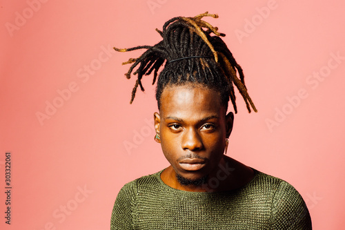 Portrait of a serious  young man in with cool dreadlocks hairstyle looking at camera, isolated on pink. photo