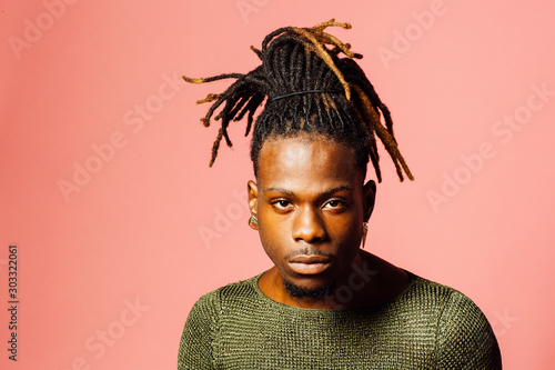 Obraz na płótnie Portrait of a serious  young man in with cool dreadlocks hairstyle looking at camera, isolated on pink