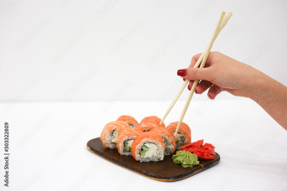 A female hand with red nails takes Philadelphia roll with chopsticks. Philadelphia rolls on white table. Japanese food. Place for text A female hand with red nails takes Philadelphia roll with chopsticks. Philadelphia rolls on white table. Japanese food. Place for text