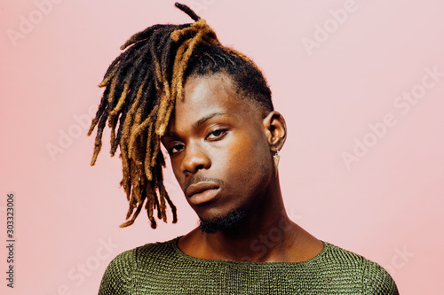 Portrait of a serious  young man in with cool dreadlocks hairstyle, isolated on pink. photo