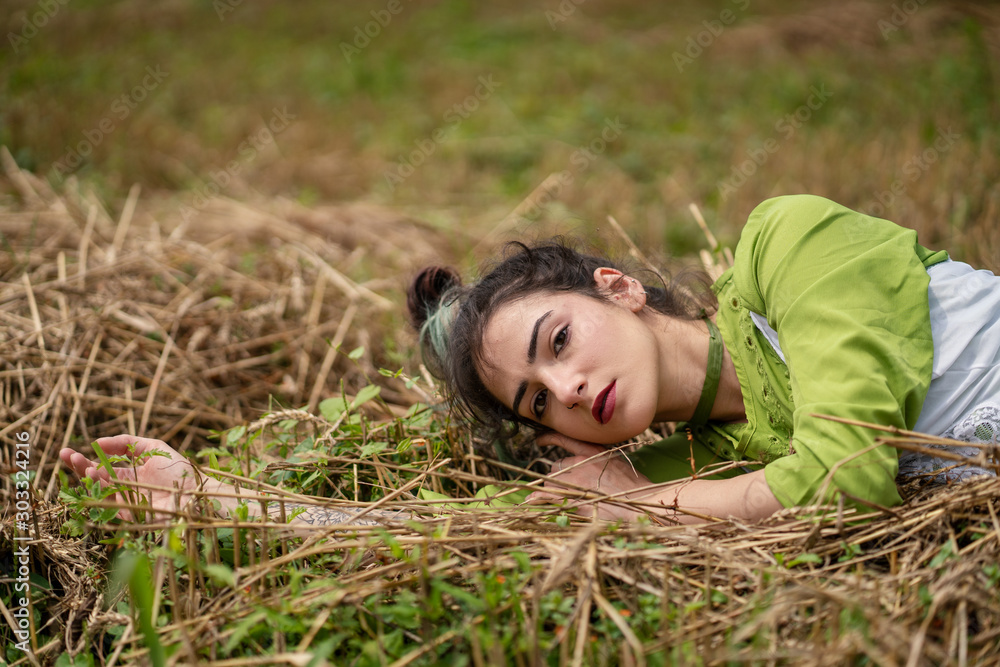 Girl lying in a wheat field and posing on hay dry grass, summer season. Relaxing in nature. Young woman posing in field. Mindset reset Girl lying in a wheat field and posing on hay dry grass, summer season. Relaxing in nature. Young woman posing in field. Mindset reset