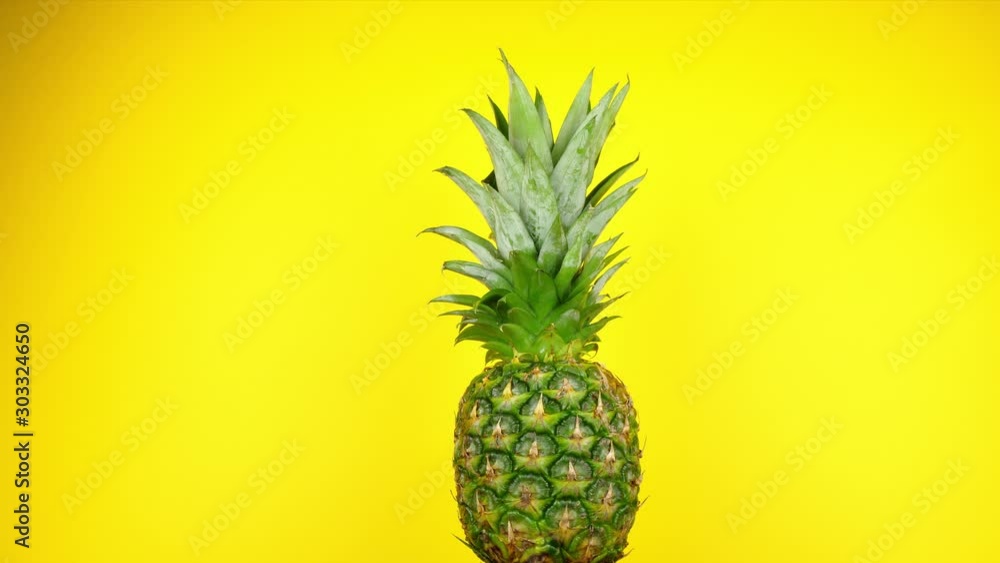 A large pineapple rotates slowly in front of a fun yellow studio background A large pineapple rotates slowly in front of a fun yellow studio background