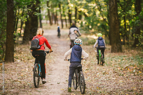 Fototapeta Naklejka Na Ścianę i Meble -  parents and kids cycling on forest trail. Young family cycling in autumn park. Family mountain biking on forest. Theme family active sports outdoor recreation. Family Cycling Through Fall Woodland