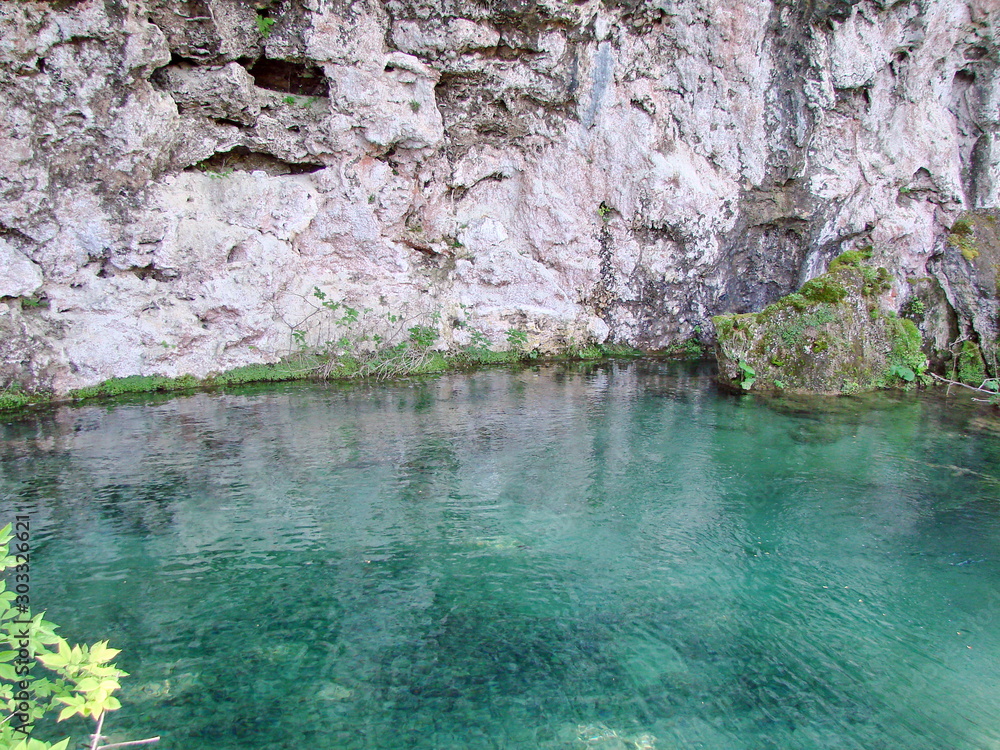 Panorama of the azure surface of a crystal clear lake surrounded by a high wall of mountain rock.