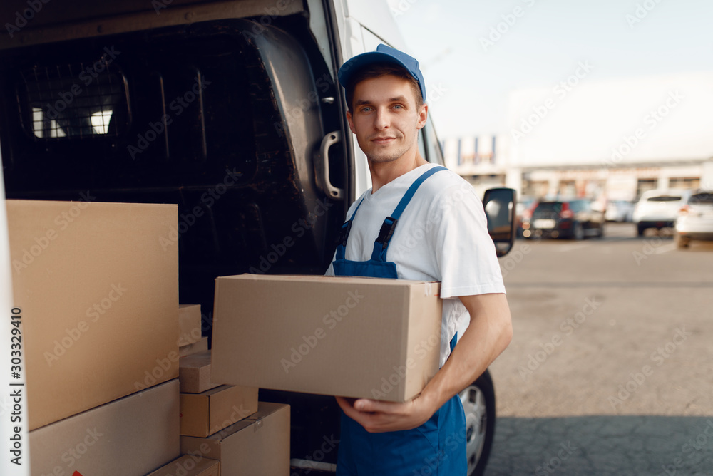 Smiling deliveryman with carton box at the car Smiling deliveryman with carton box at the car