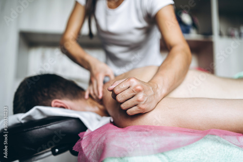 Female masseuse gives back massage to man who is lying on massage couch