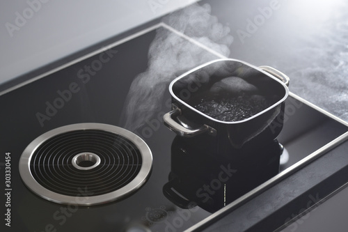 Bild auf Leinwand Modern electric induction cooker with built-in ventilation and extractor hood which draws steam from boiling water in a pan