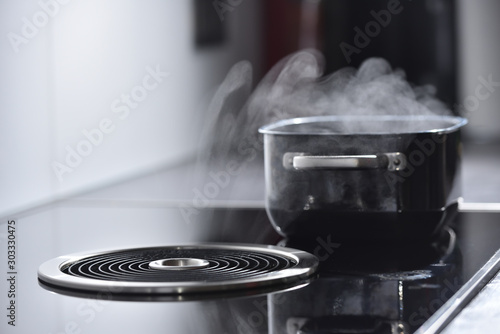 Modern electric induction cooker with built-in ventilation and extractor hood which draws steam from boiling water in a pan. Steam from a boiling pot is drawn into the integrated range hood photo