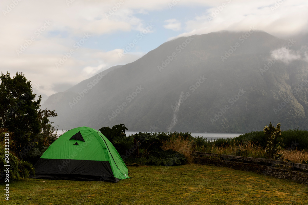 Green camp tent against mountains in a foggy day in Caleta Gonzalo, Pumalin Park, Chaiten, Patagonia, Chile