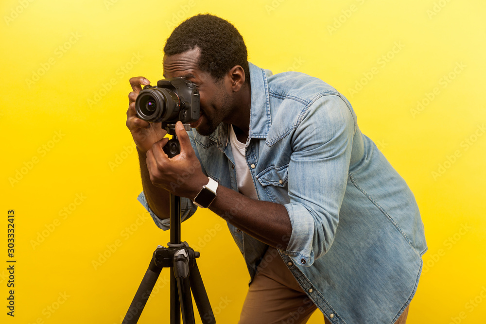Φωτογραφία Portrait of happy photographer enjoying his job or traveler in denim casual shirt taking picture with professional digital dslr camera on tripod