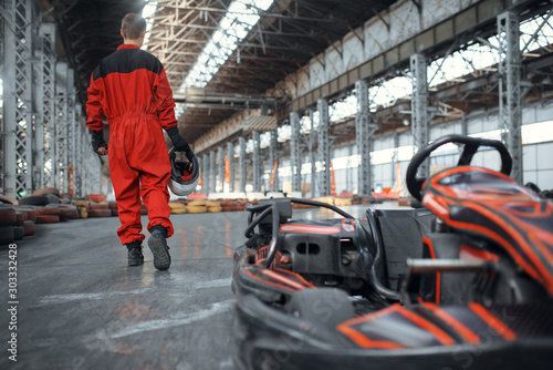 Racer with helmet near go kart car, back view