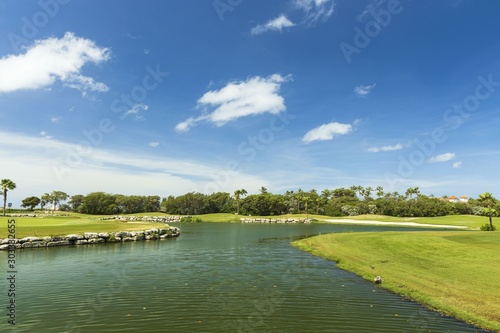 Beautiful tropical natural landscape view. Green grass field and pond water surface on blue sky with rare white clouds background.