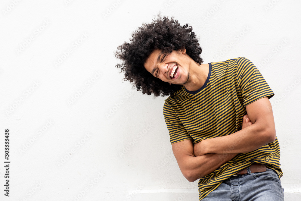 Cool young handsome man with afro hair laughing with arms crossed by white background