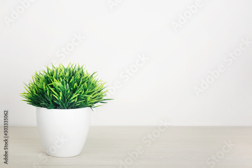 Artificial grass in a pot on a wooden table on a white background. The concept of office interior, home comfort, lifestyle. Mock-up with copy space for your text.