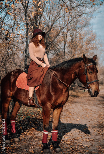 Beautiful red haired woman posing on horse outdoor.