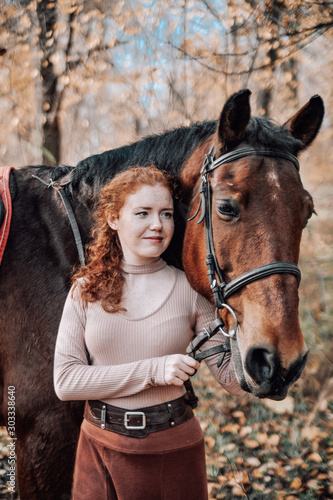 Portrait of beautiful red haired woman with horse outdoors.