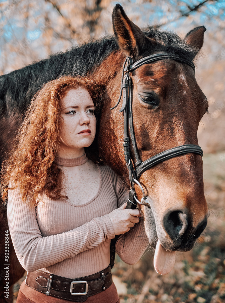 Fototapeta premium Portrait of beautiful red haired woman with horse outdoors.