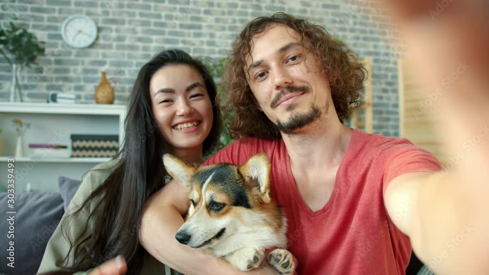 Joyful girl and guy taking selfie with corgi dog having fun making funny faces showing hand gestures thumbs-up and v-sign. Youth and technology concept. Joyful girl and guy taking selfie with corgi dog having fun making funny faces showing hand gestures thumbs-up and v-sign. Youth and technology concept.