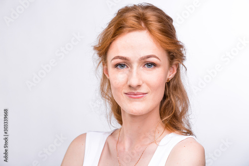 Portrait of a beautiful young woman of European, Caucasian nationality with long red hair and freckles on her face posing on a white background in the studio. Close-up student girl in a white blouse